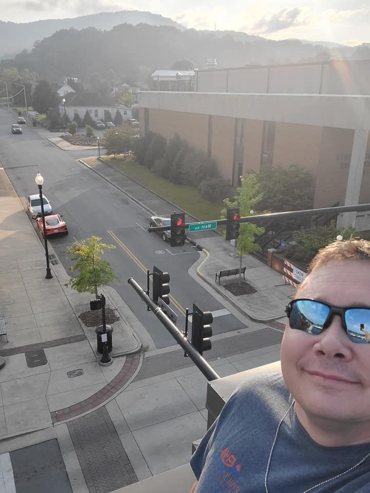 A man wearing sunglasses is standing on a balcony overlooking a city street.