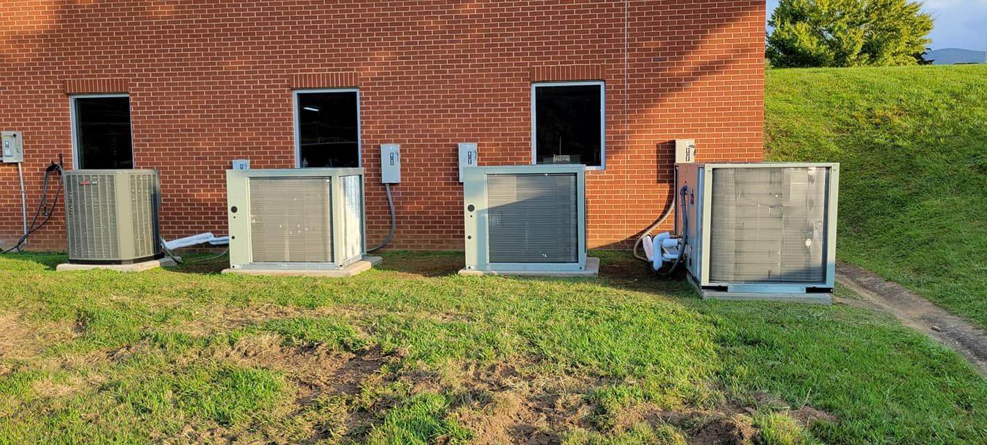 Three air conditioners are sitting in front of a brick building.