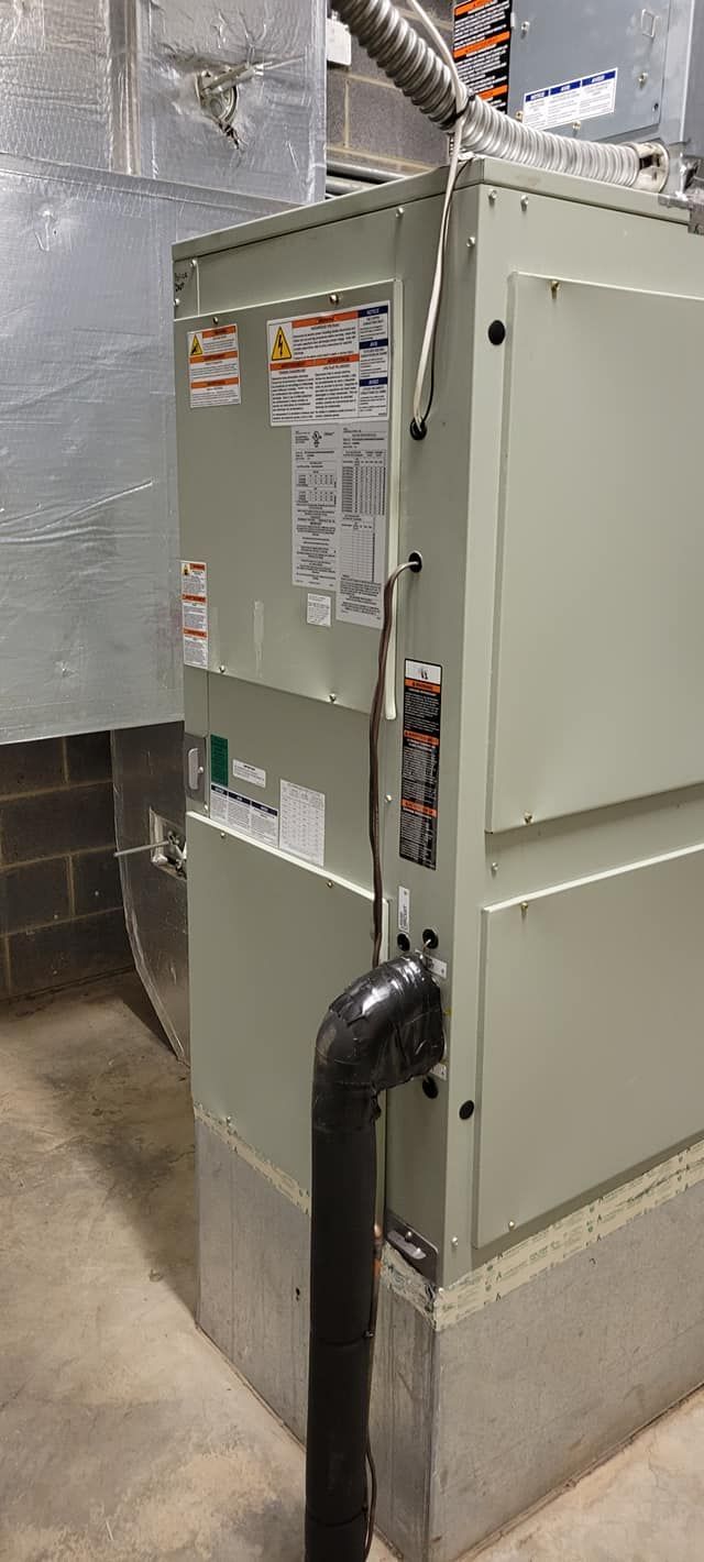 An air conditioner is sitting in a basement next to a pipe.