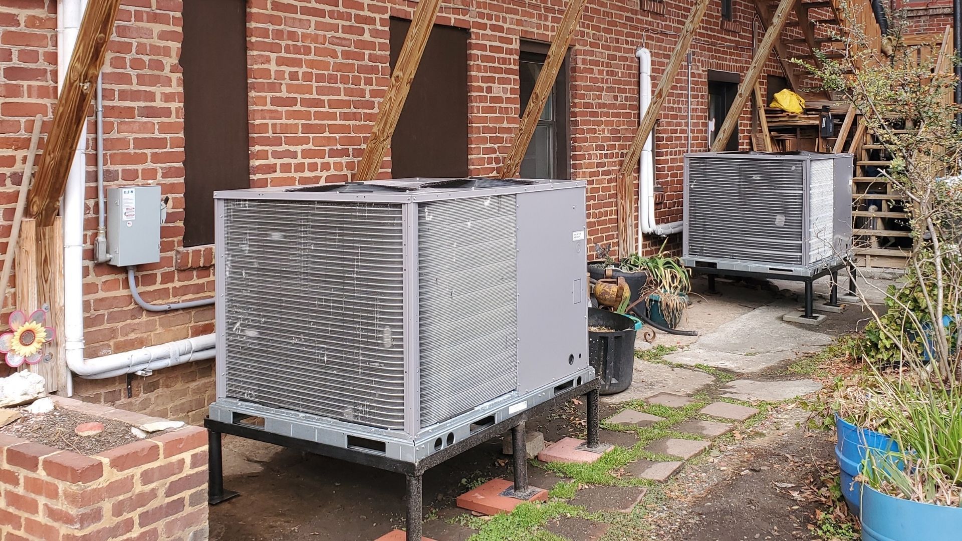 Two air conditioners are sitting outside of a brick building.