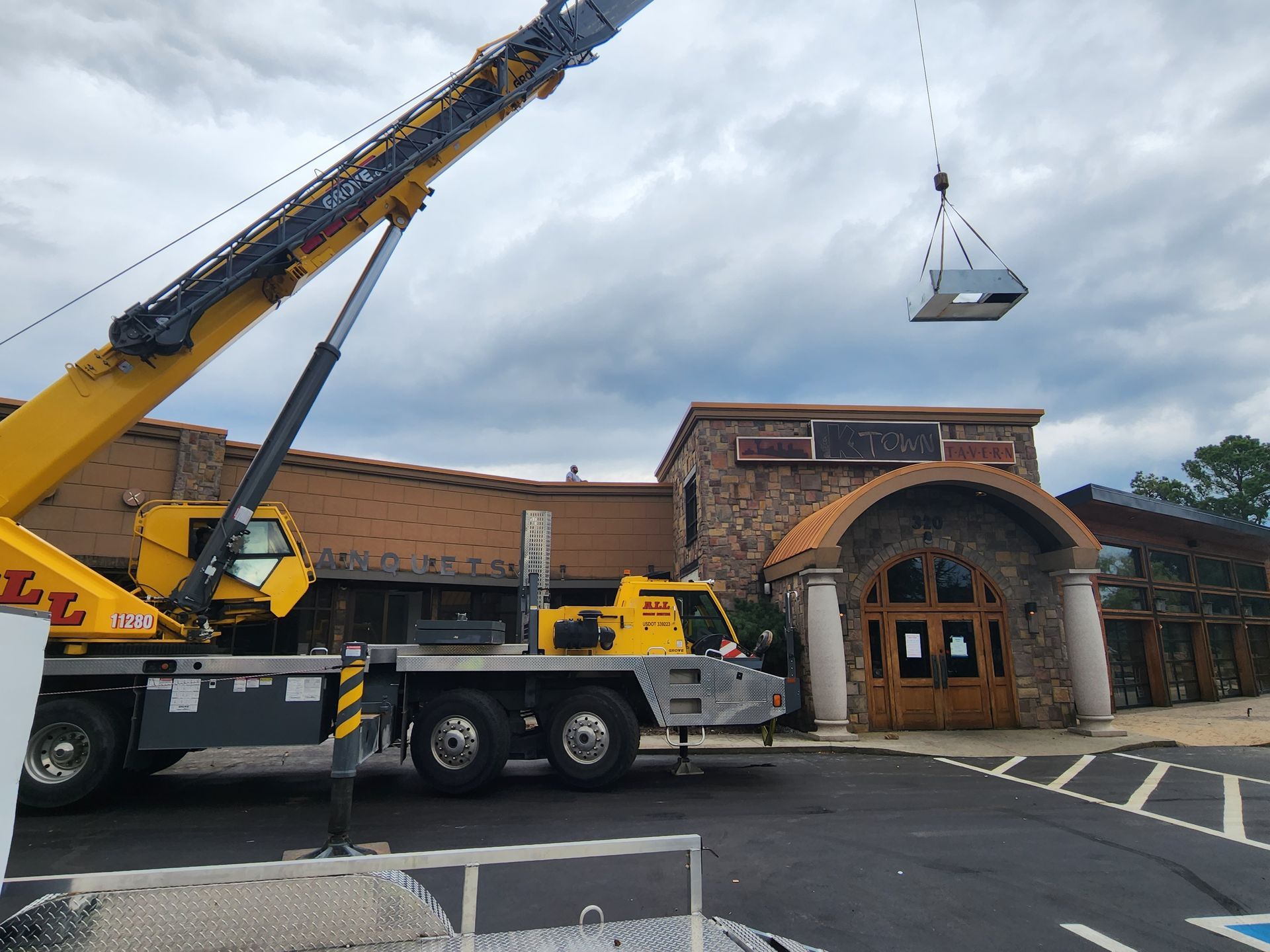 A yellow truck with a crane attached to it is parked in front of a building