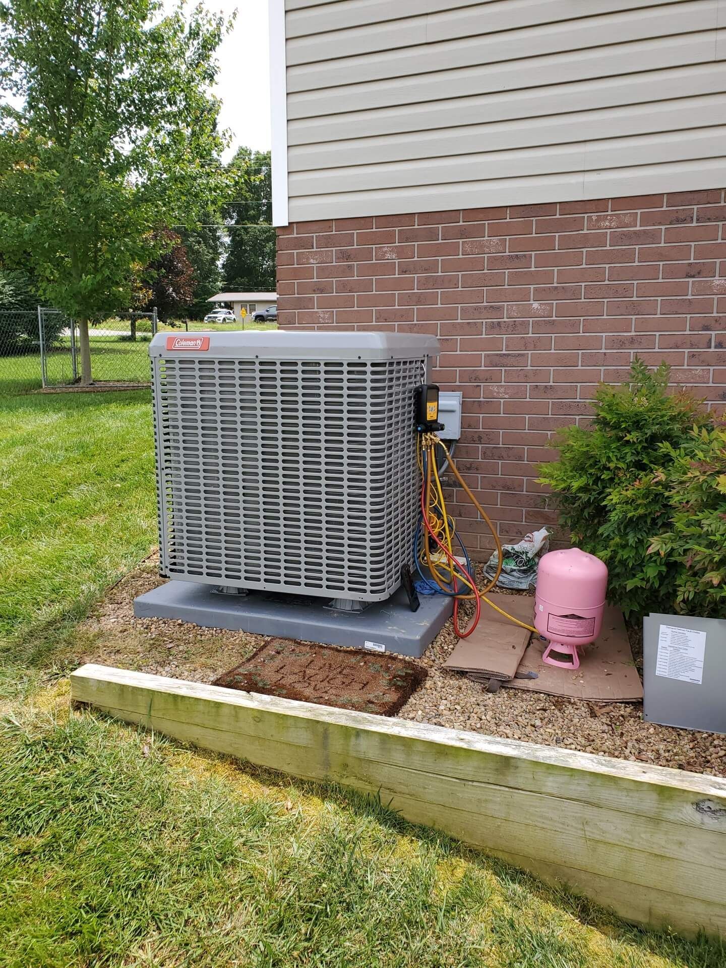 An air conditioner is sitting on the side of a brick house.