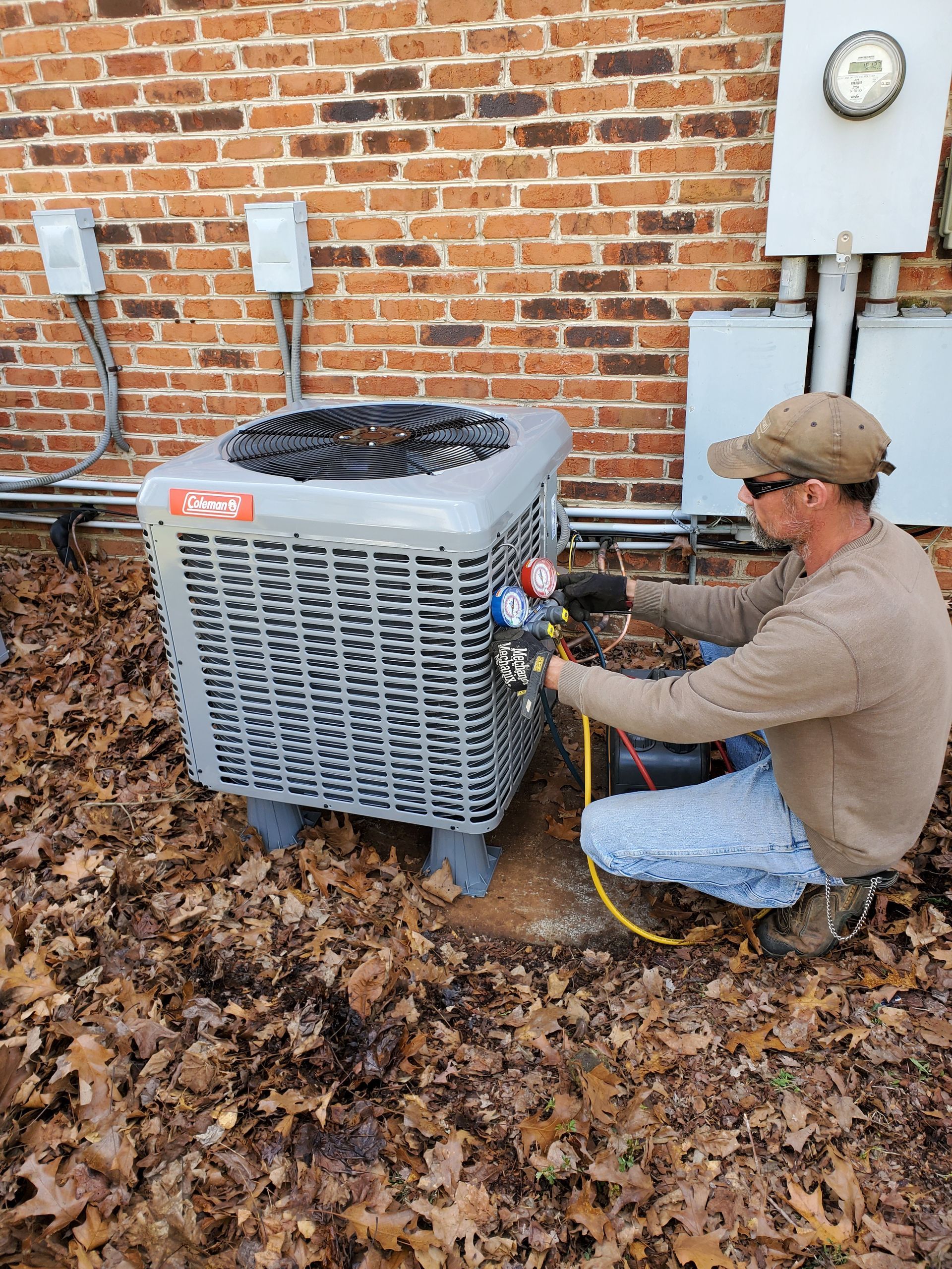 A man is working on an air conditioner outside of a brick building.