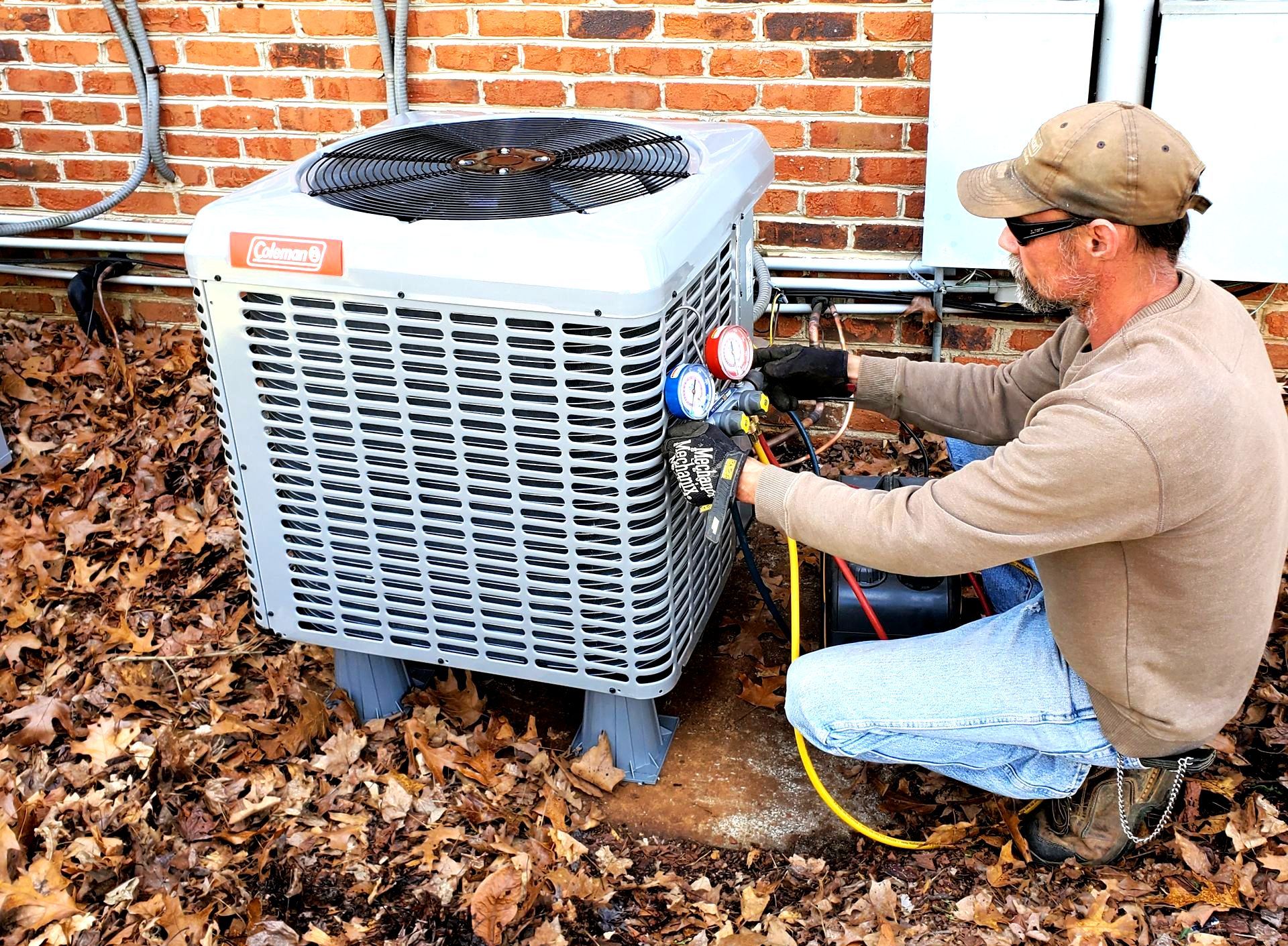 A man is working on an air conditioner outside of a brick building.