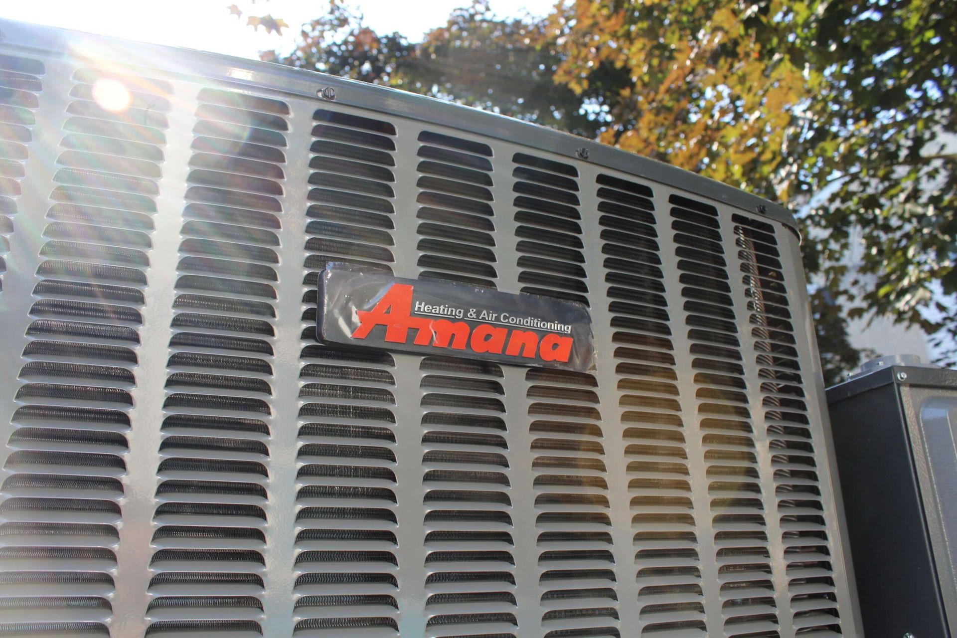 A close up of a amana air conditioner with trees in the background