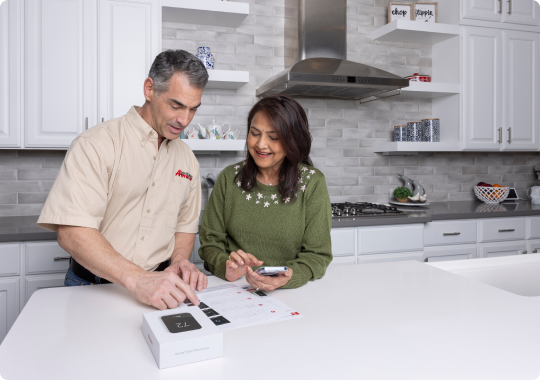 A man and a woman are sitting at a kitchen counter looking at a box.