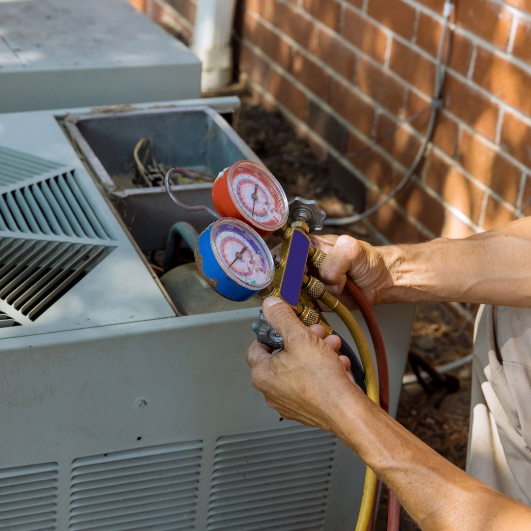 A person is holding two gauges in front of an air conditioner.