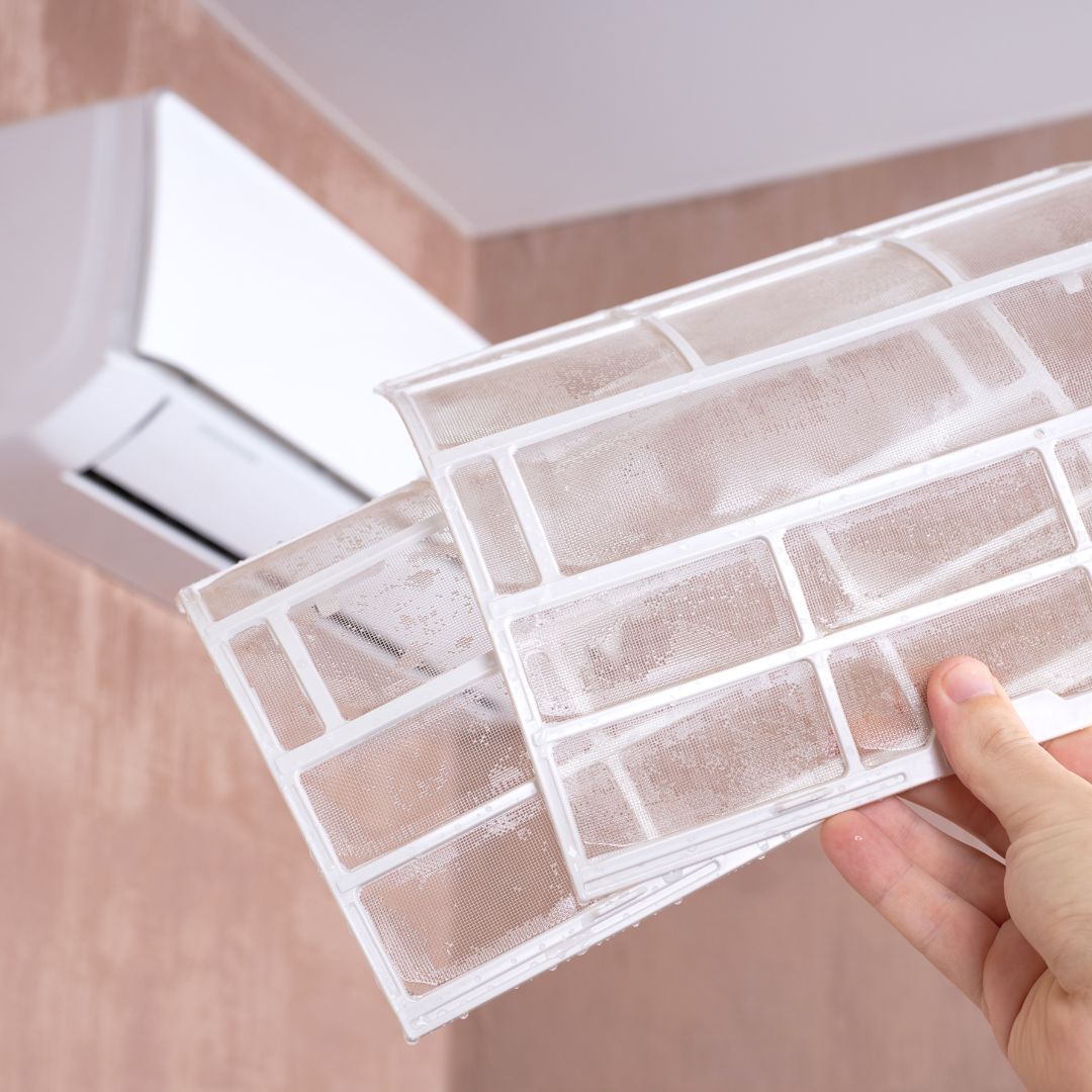 A person is holding a filter in their hand in front of an air conditioner.