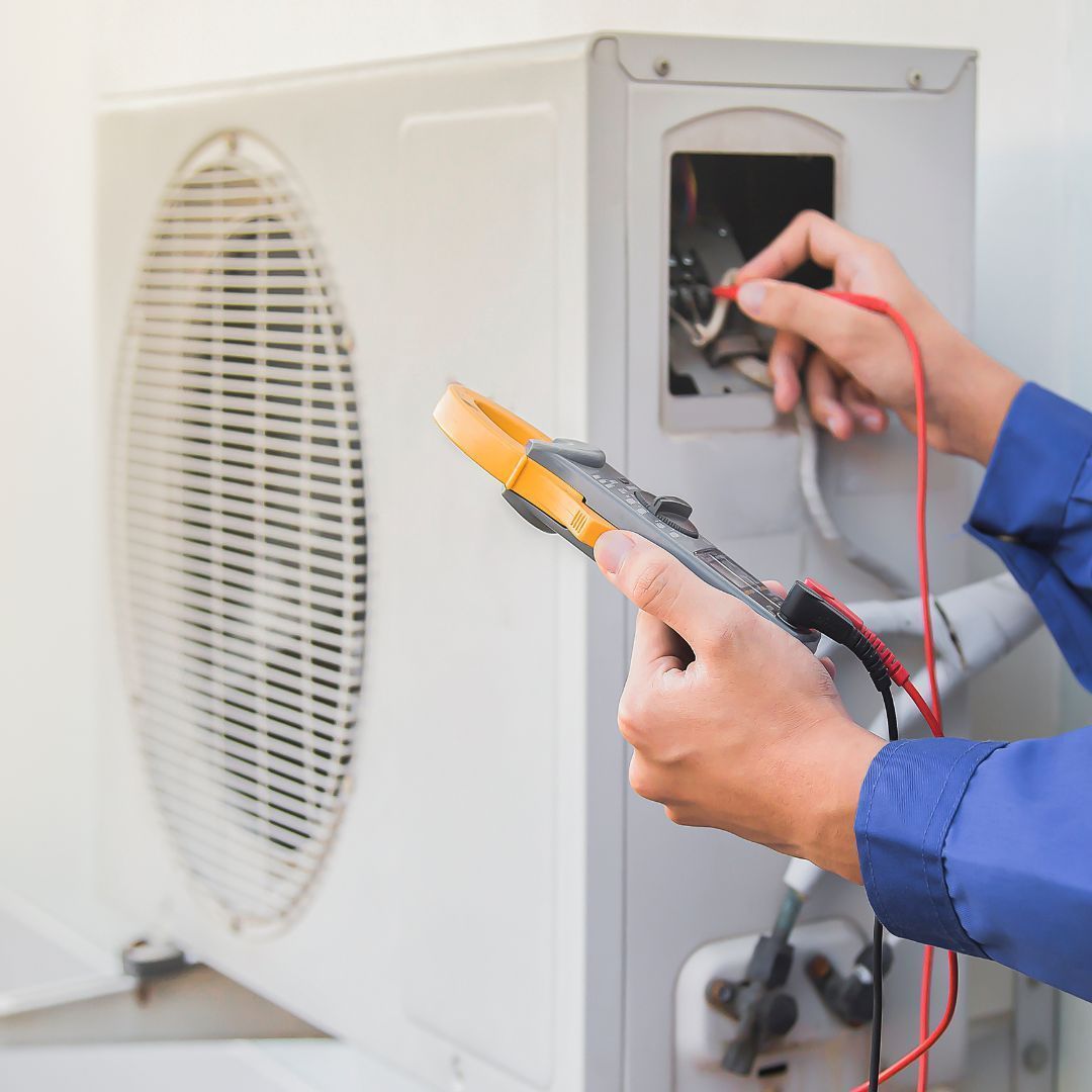 A person is working on an air conditioner with a pair of pliers