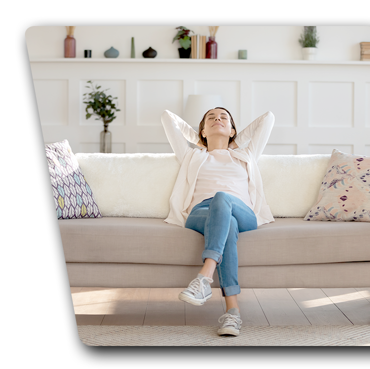 A woman is sitting on a couch with her hands behind her head