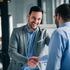 A man in a suit is shaking hands with another man in a blue shirt.