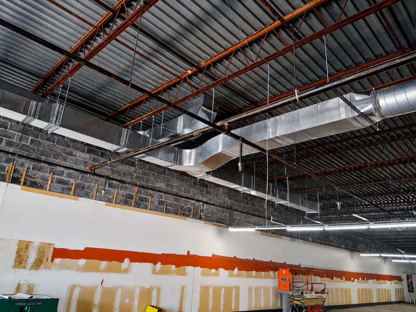 Industrial warehouse interior with exposed ceiling beams, white walls, and orange paint markings on the far wall
