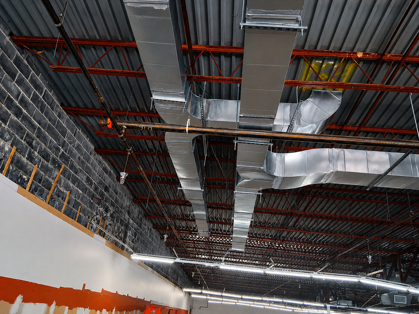 Industrial ceiling with exposed red pipes, silver ductwork, and insulated panels in a building under construction
