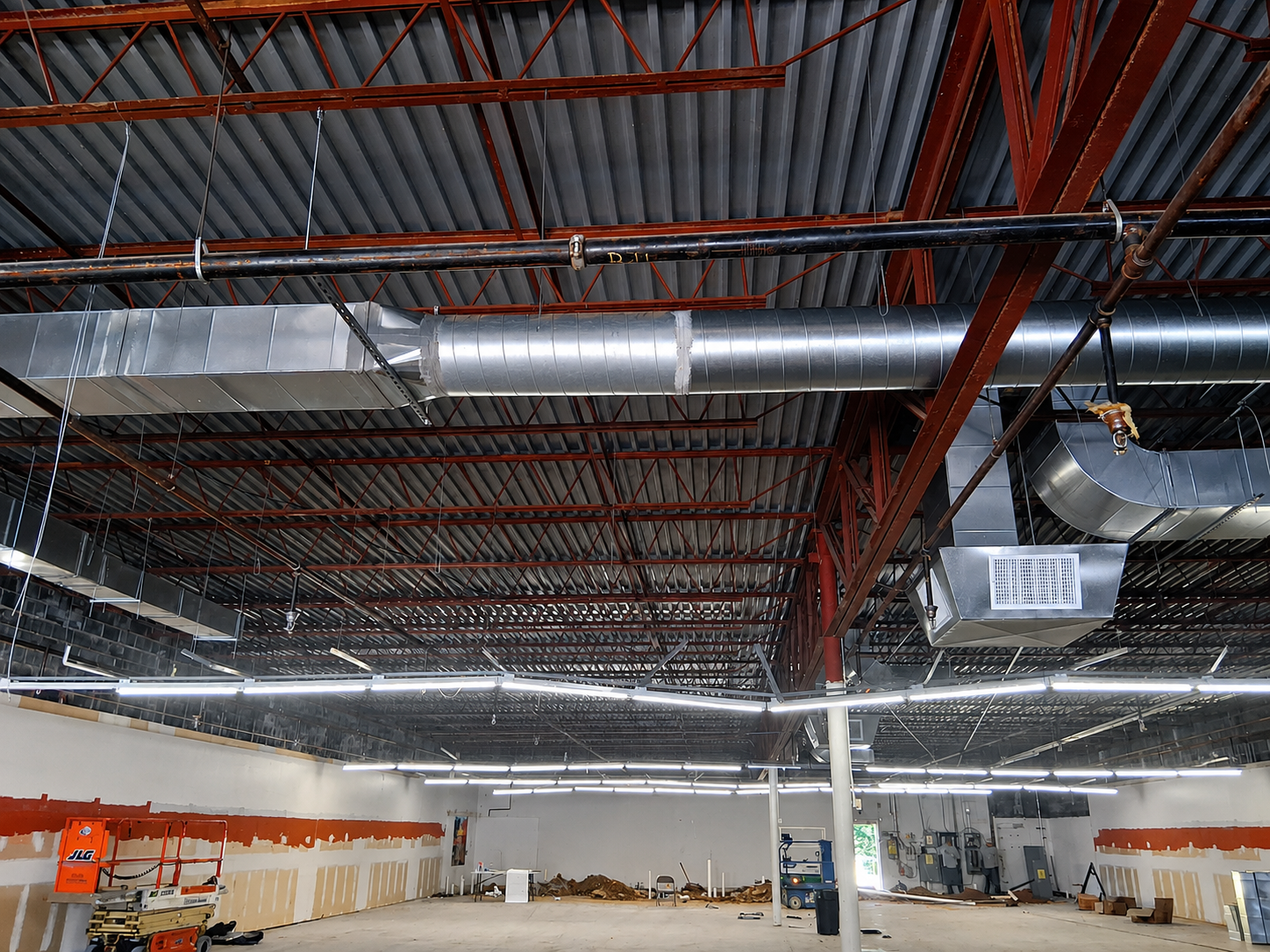 Industrial warehouse interior with exposed red ceiling beams, silver ductwork, and bright overhead lights