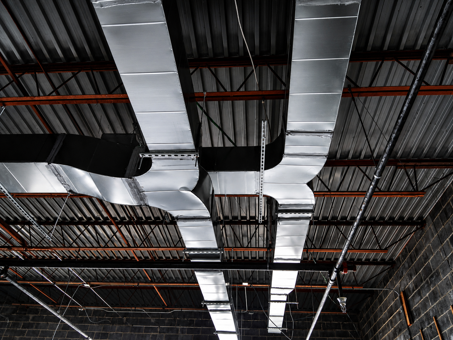 Industrial ceiling with silver HVAC ducts and exposed black beams overhead