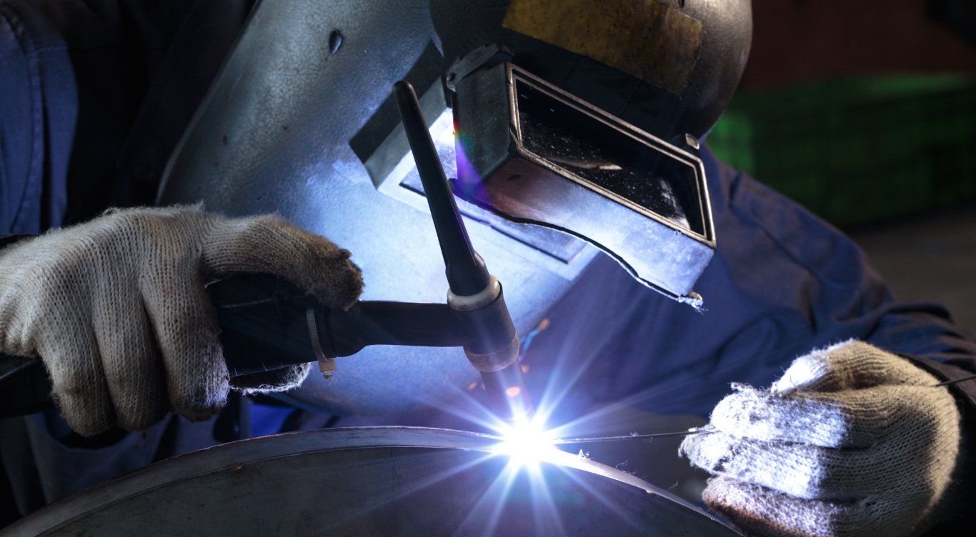 A man wearing a welding helmet is welding a piece of metal.