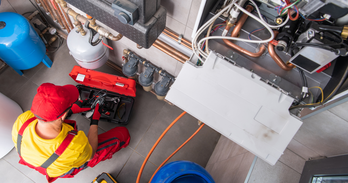 Plumber in red and yellow working on heating system with tools.