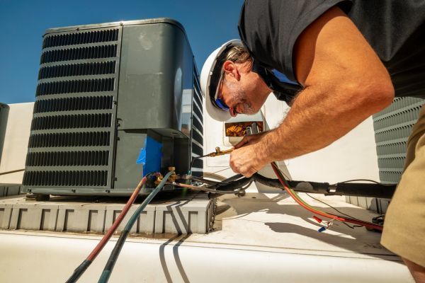 A man is working on an air conditioner on the roof of a building.