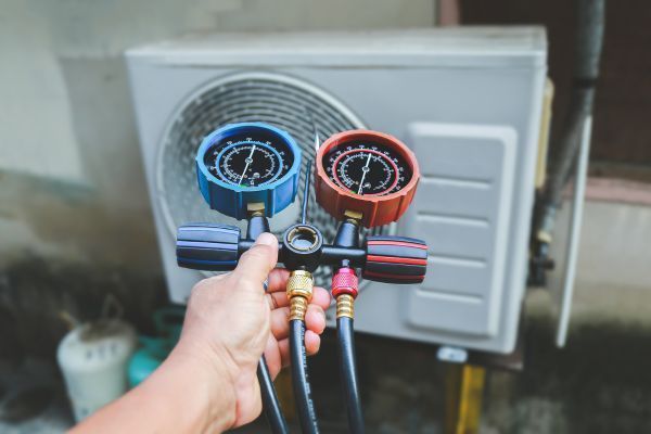 A person is holding two gauges in front of an air conditioner.