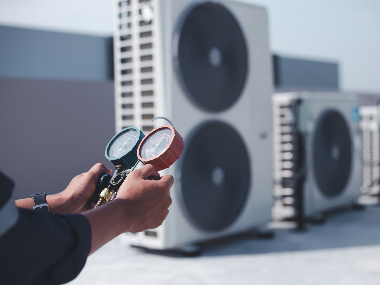 A man is holding two gauges in front of a row of air conditioners.