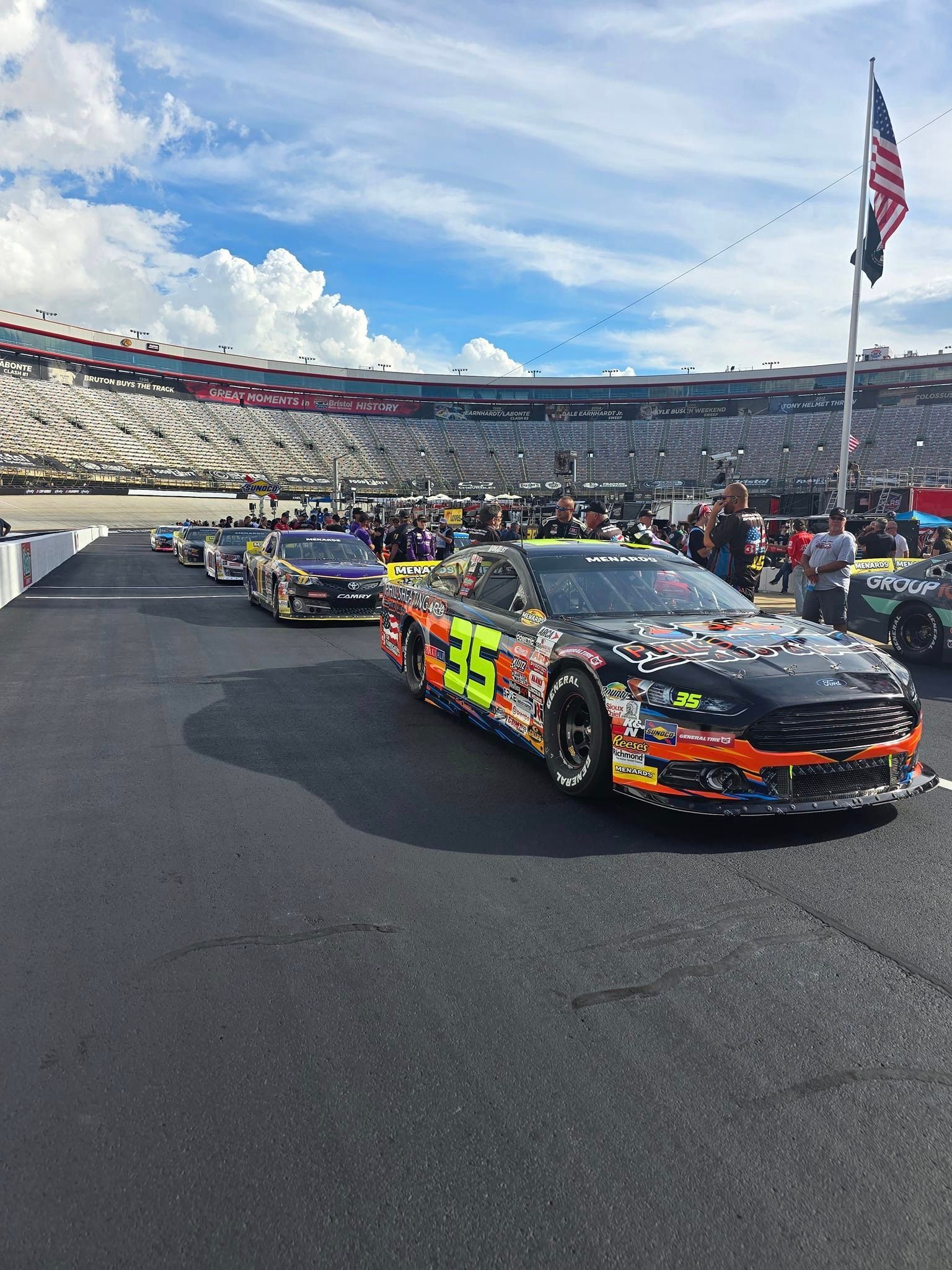 A row of race cars are parked on the side of a race track.