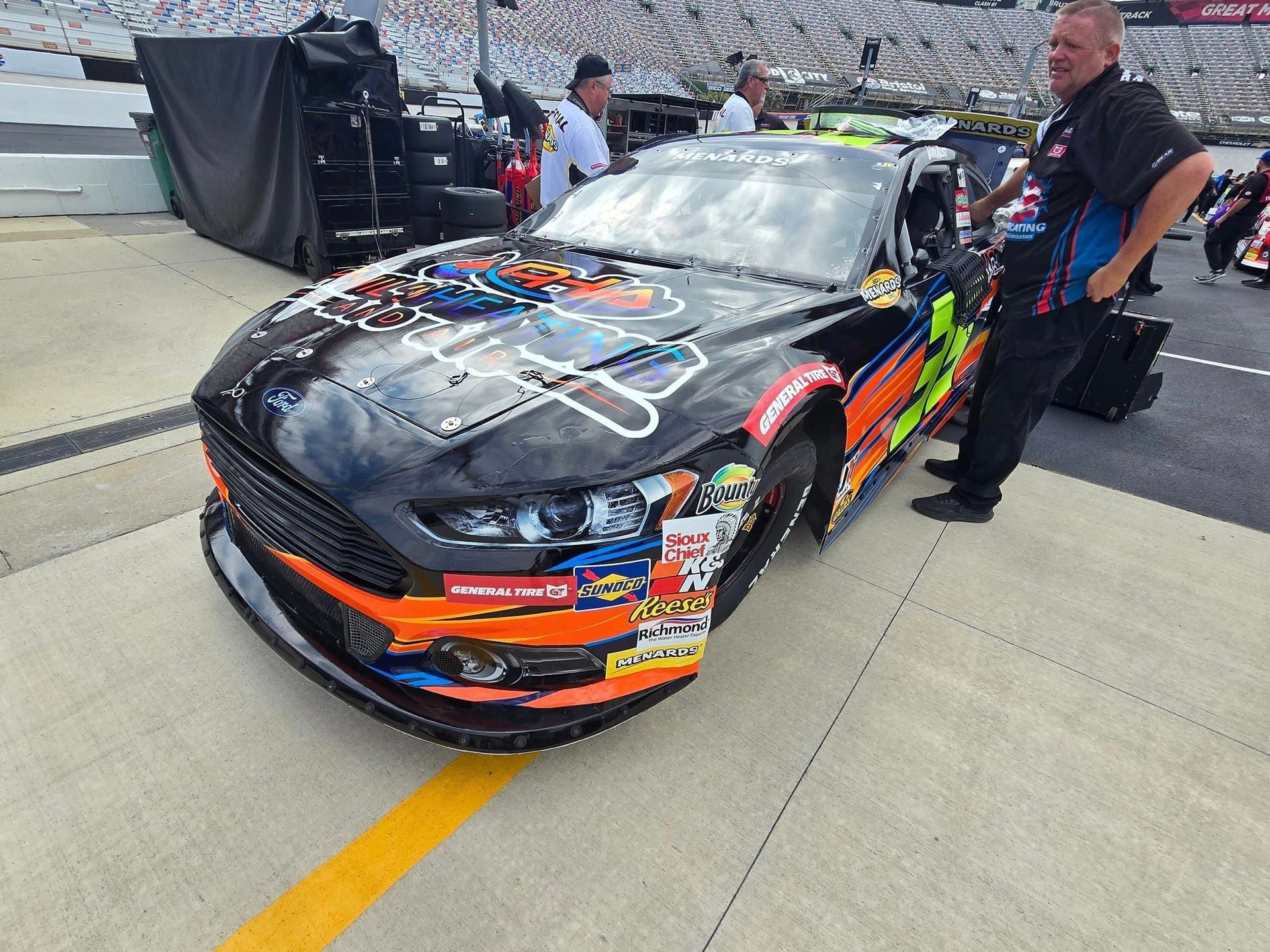 A man is standing next to a race car in a parking lot.