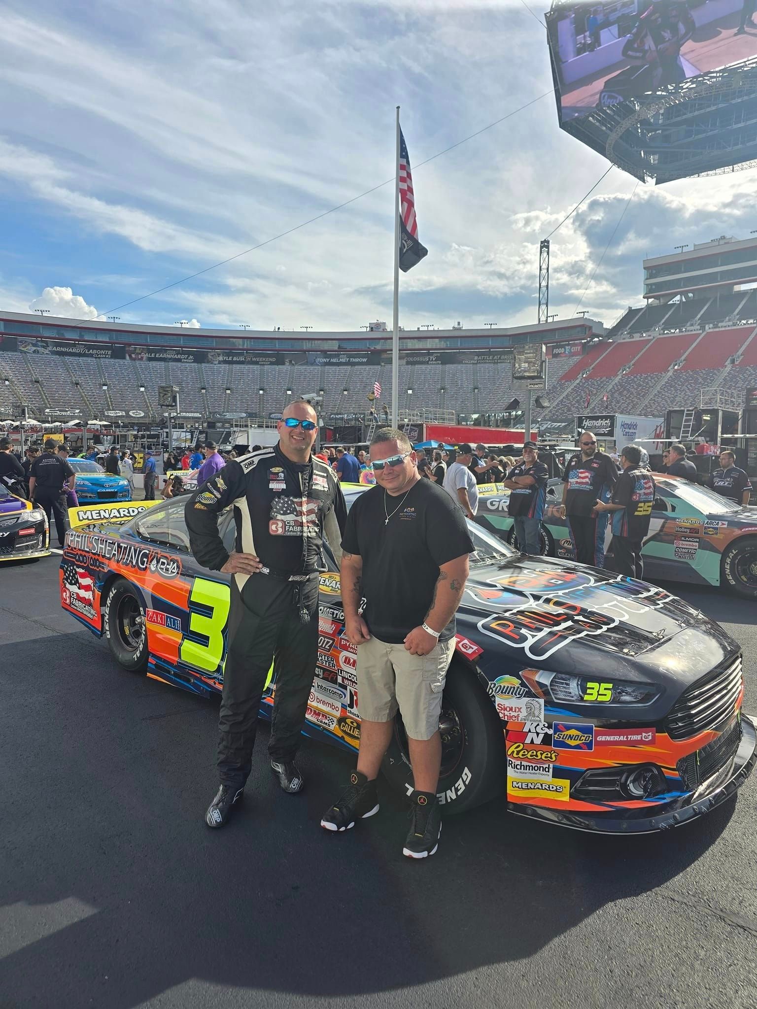 Two men are standing next to a race car at a race track.