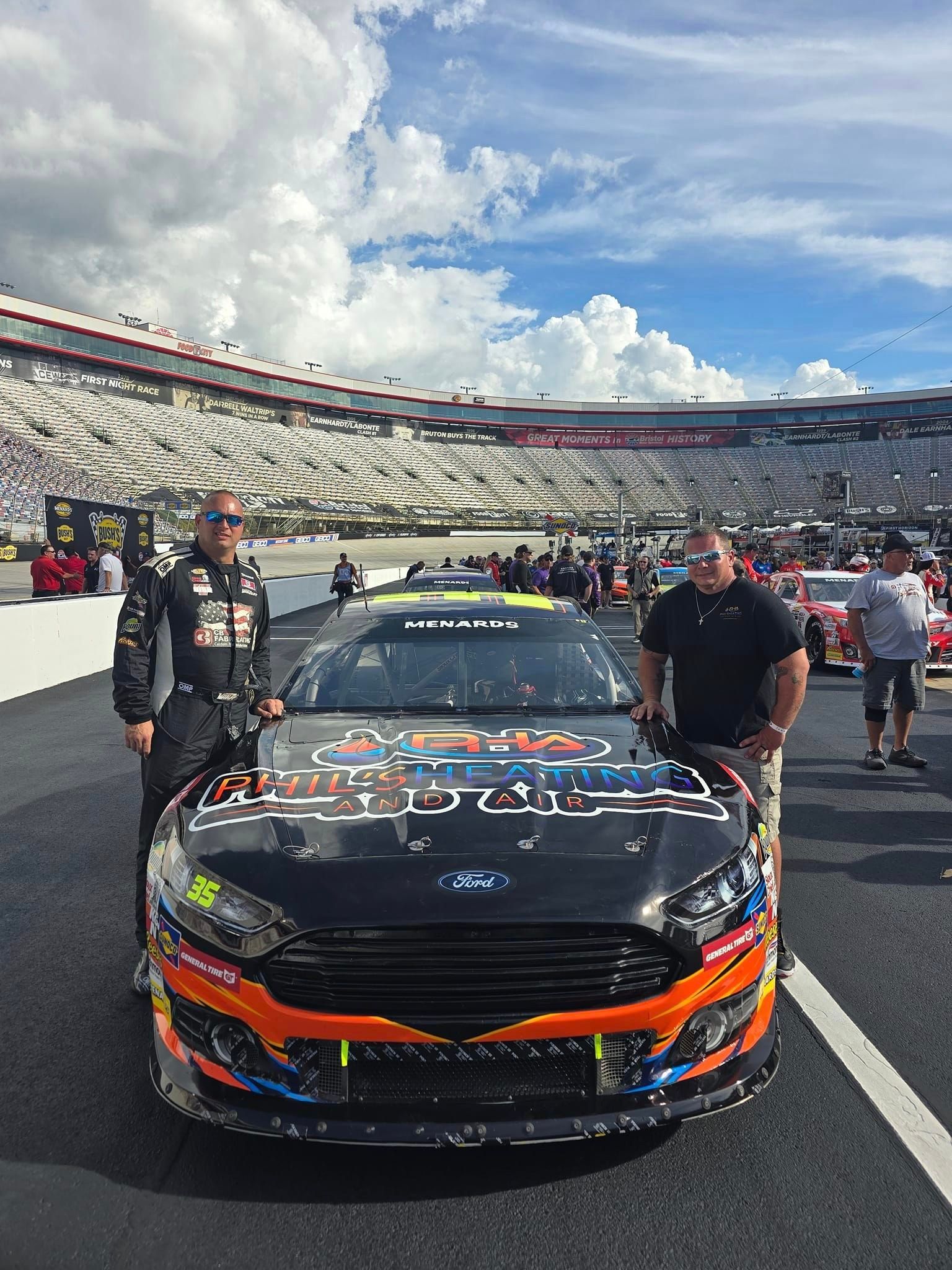 Two men are standing next to a race car on a race track.