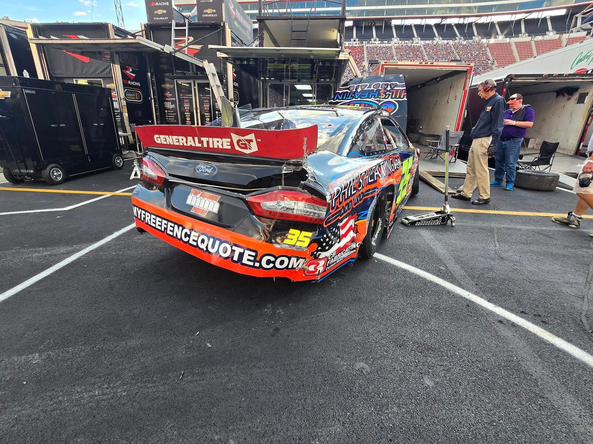 A race car is parked in a parking lot next to a trailer.