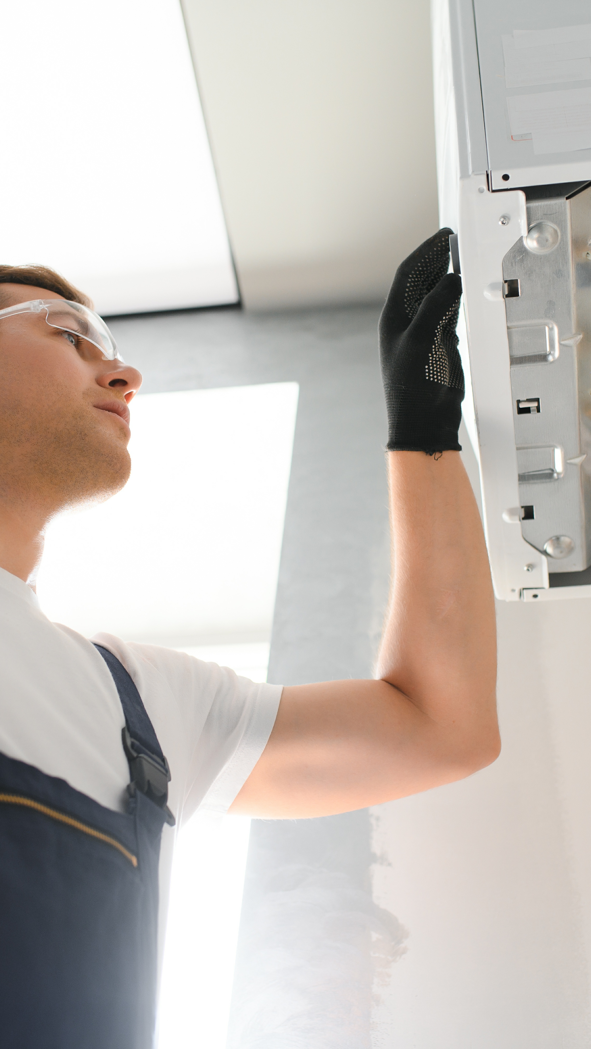 A man wearing safety glasses and gloves is working on a refrigerator.