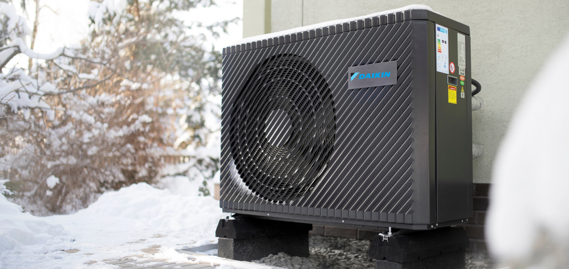 Black heat pump unit covered in snow, sitting outside in a winter setting.
