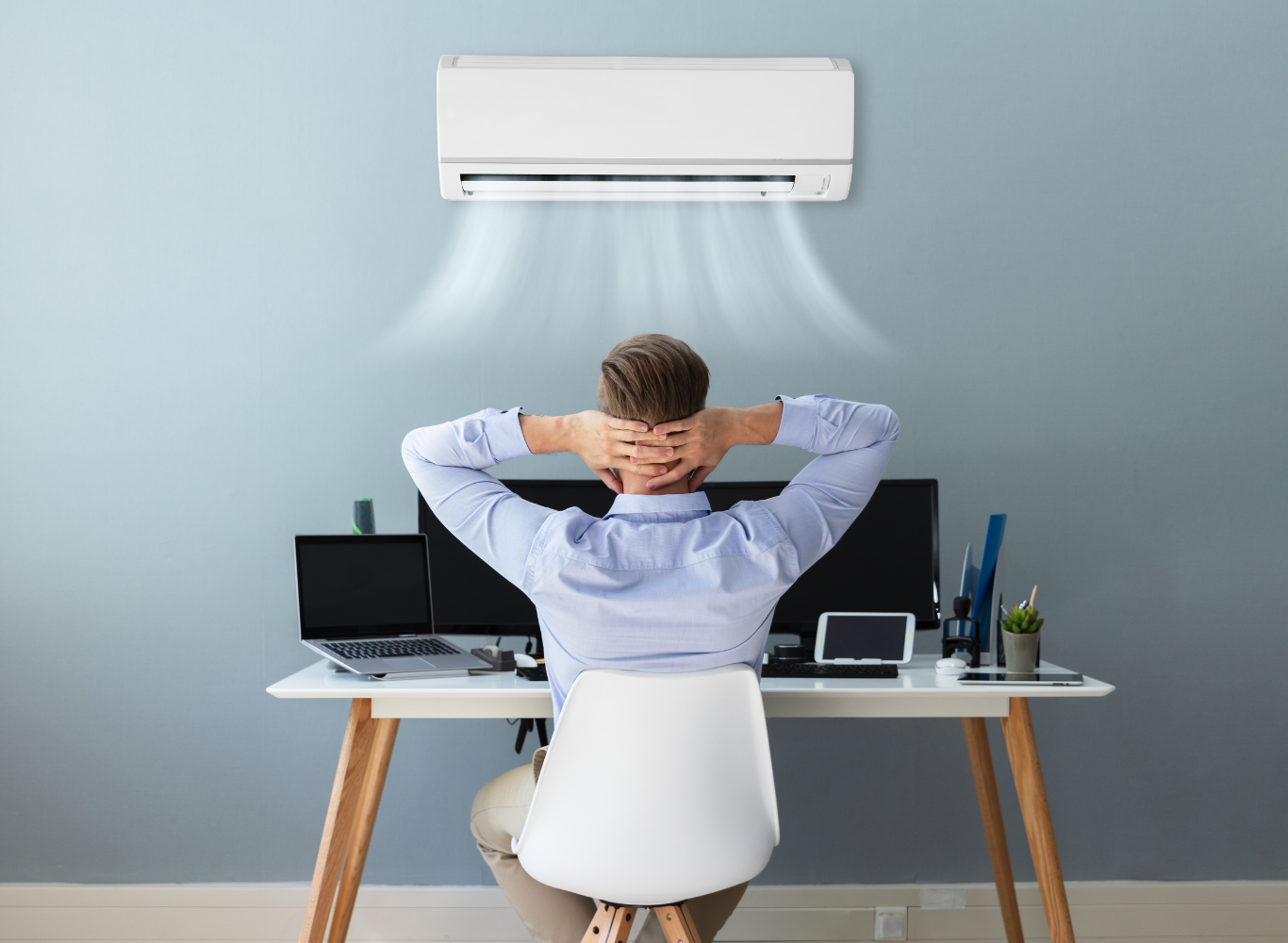 A man is sitting at a desk under an air conditioner.