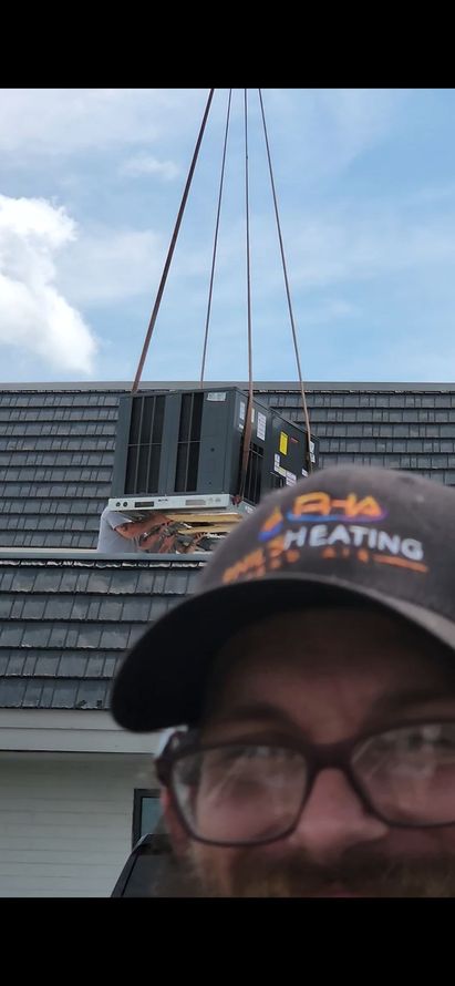 A man wearing a hat that says heating is standing on a roof.