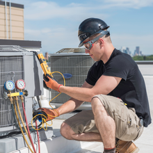 A man is working on an air conditioner on a rooftop.