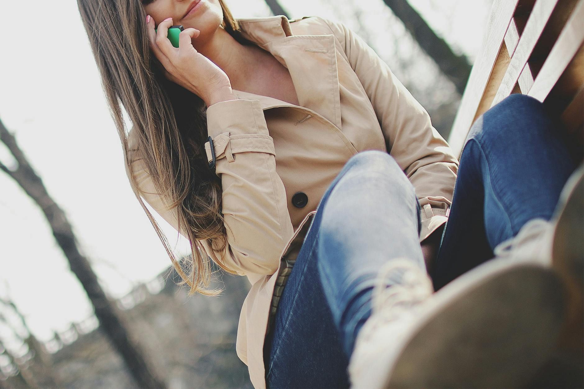 A woman in a trench coat is talking on a cell phone