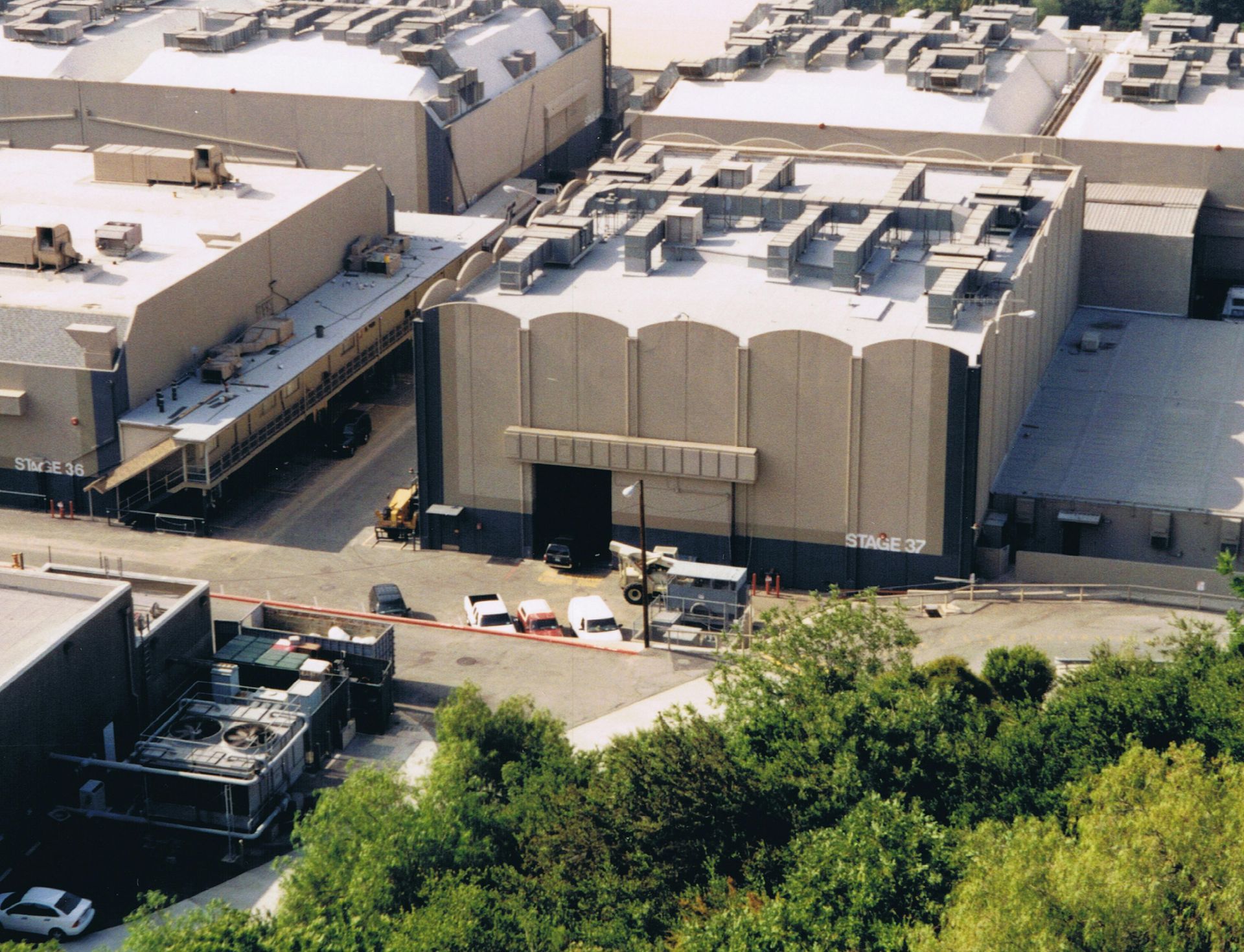 Film studio exterior with several buildings, some vehicles, and trees.
