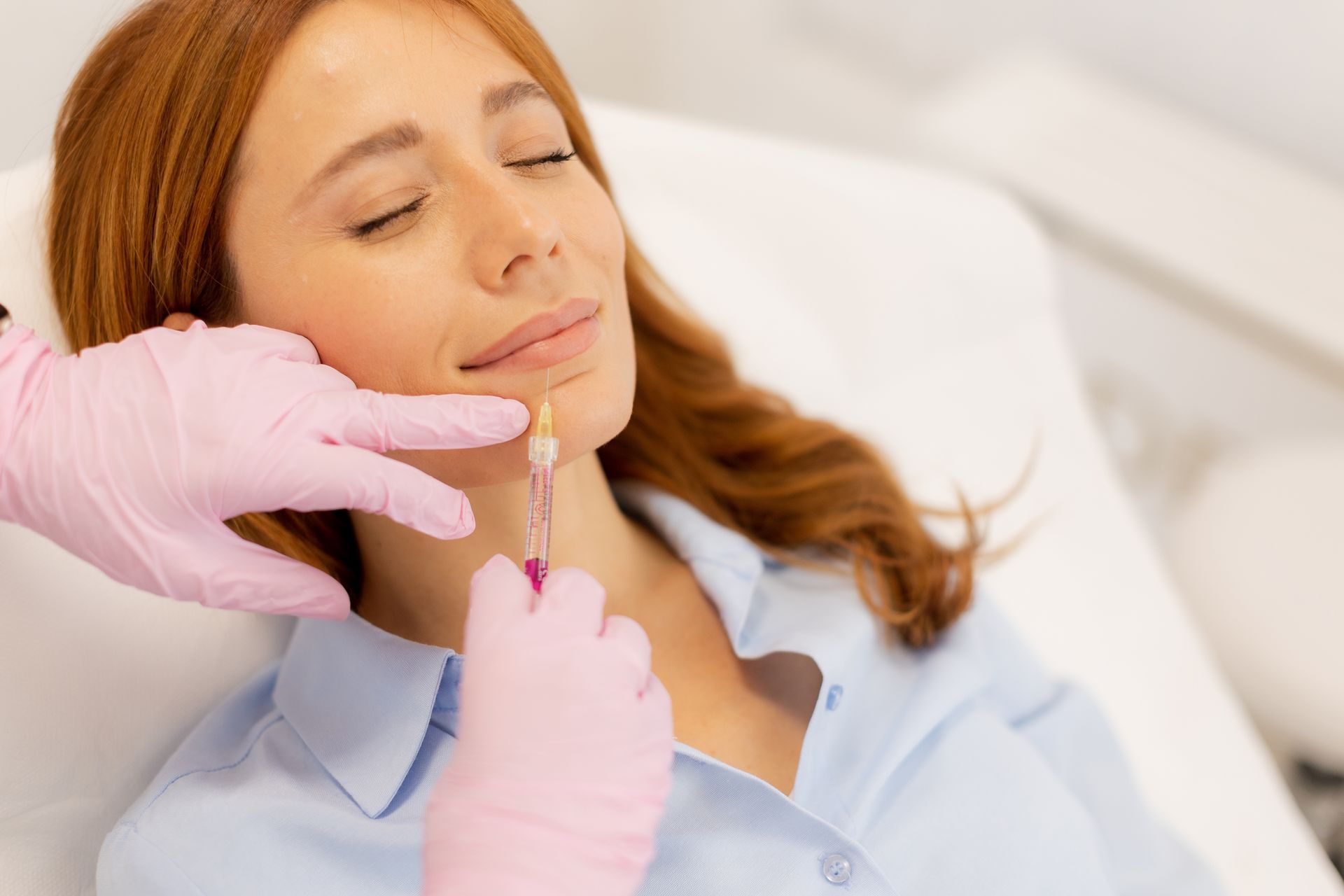 Gloved hands applying lip filler to a relaxed woman in a clinic setting
