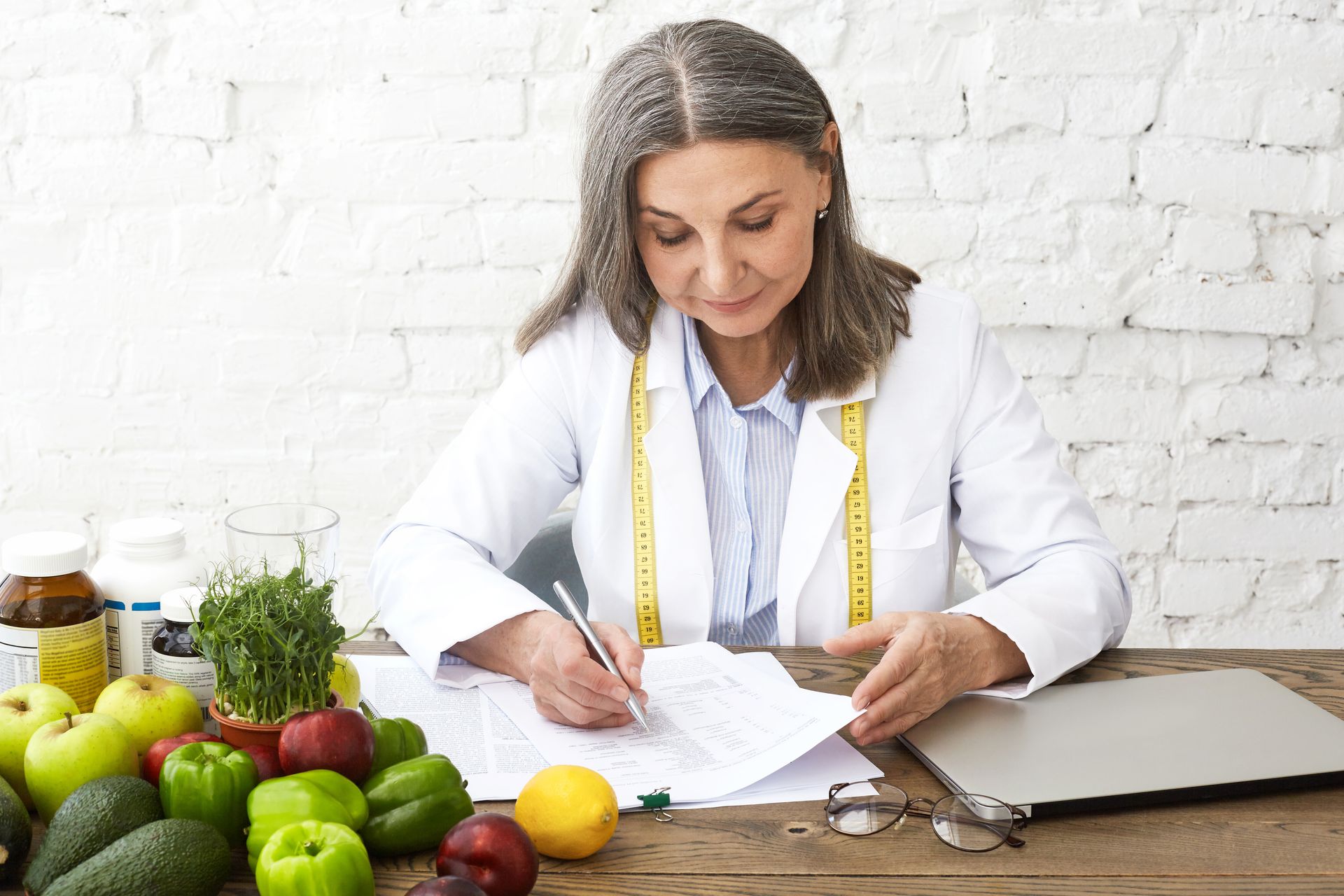 A woman is sitting at a table with fruits and vegetables and writing on a piece of paper.