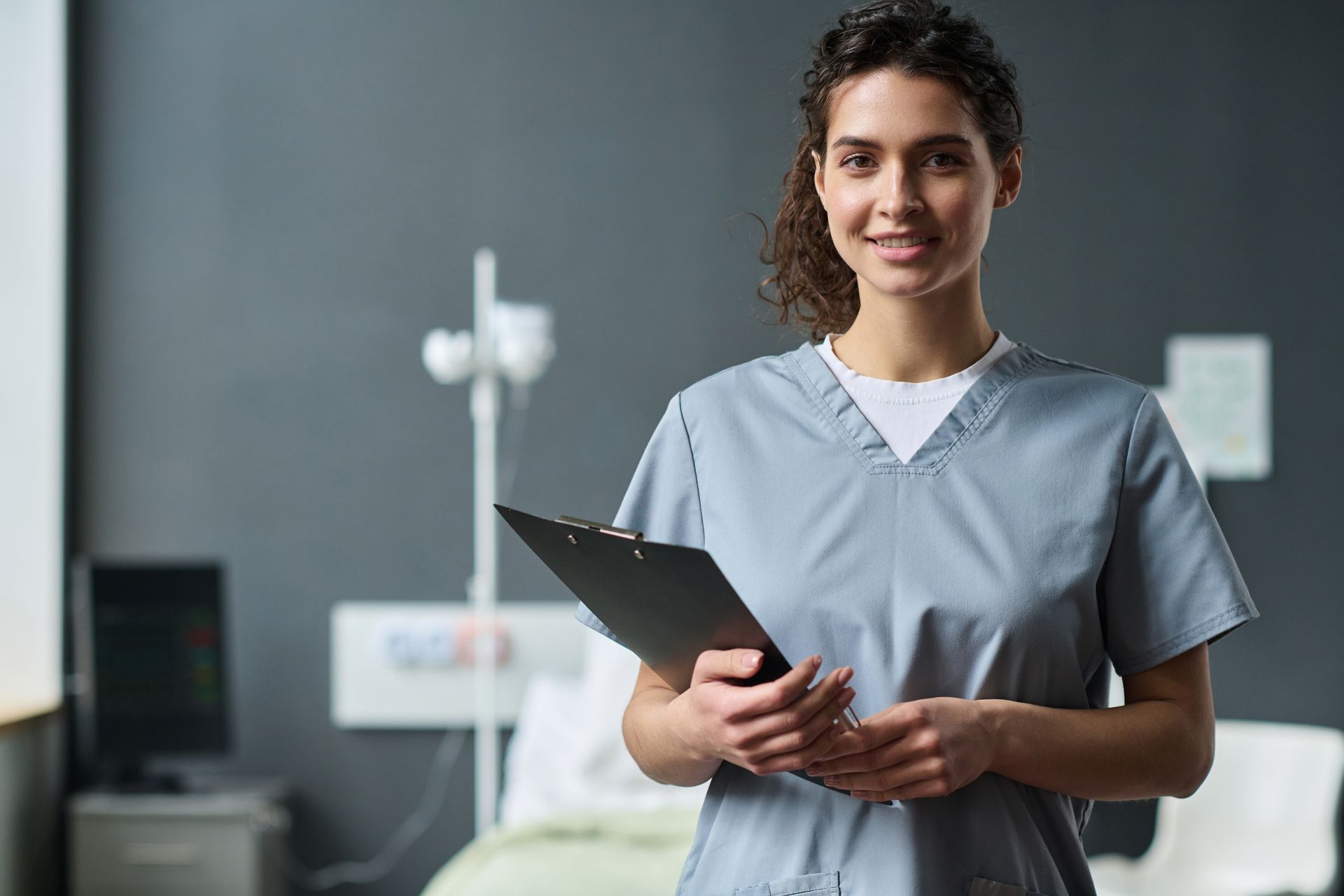 A nurse is holding a clipboard in a hospital room.