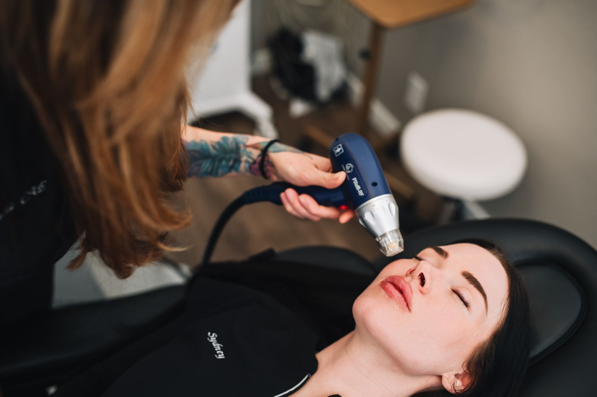 Woman receiving facial treatment with a handheld device in a clinic setting.