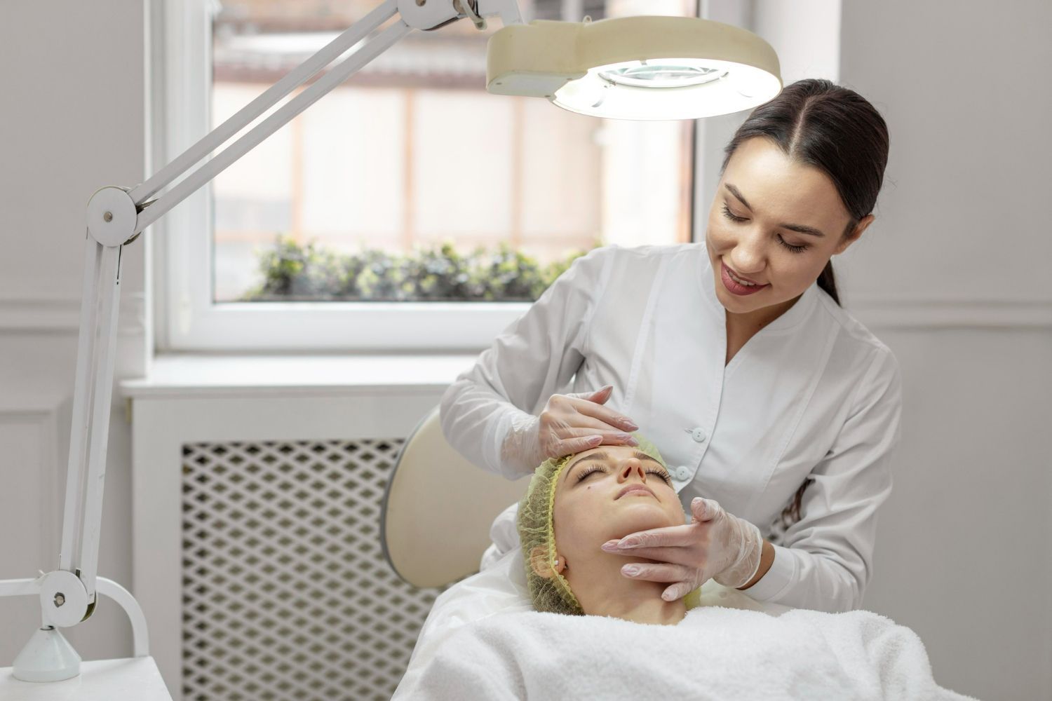 Beautician performing a facial treatment on a client in a bright, clean spa room.