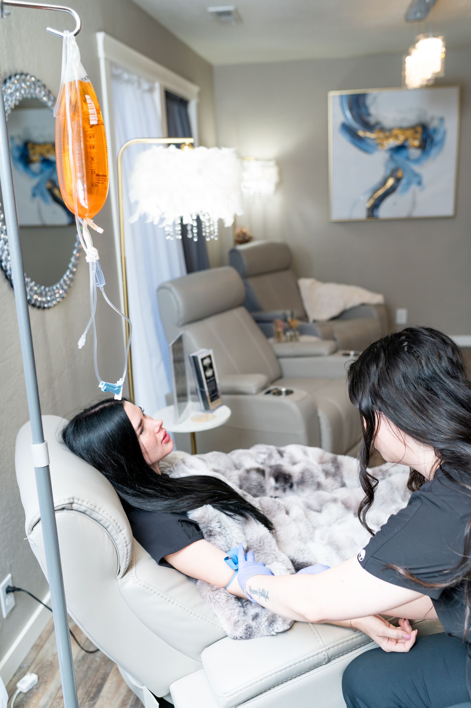 Woman receiving IV drip in a treatment room. Another person is attending to her arm.