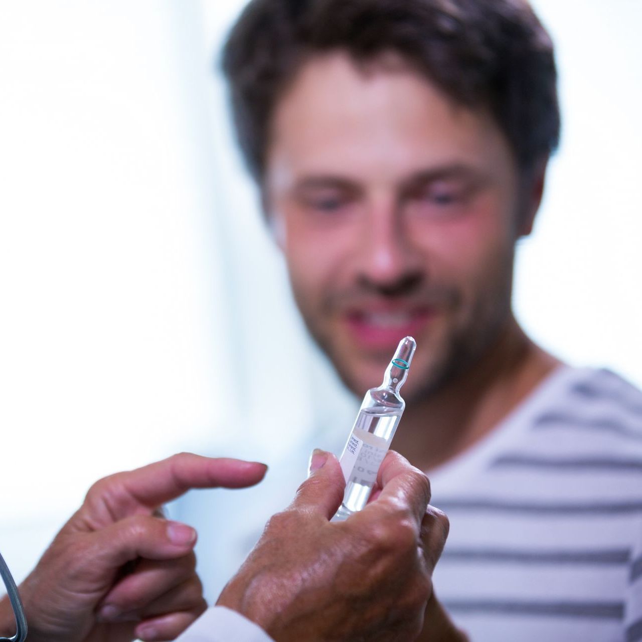 A man in a striped shirt is looking at a syringe