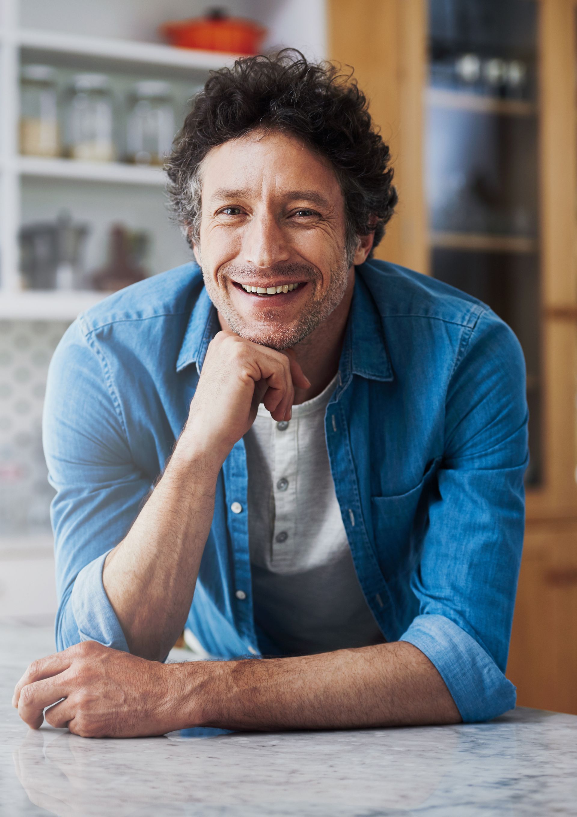 A man in a blue shirt is sitting at a table with his hand on his chin.