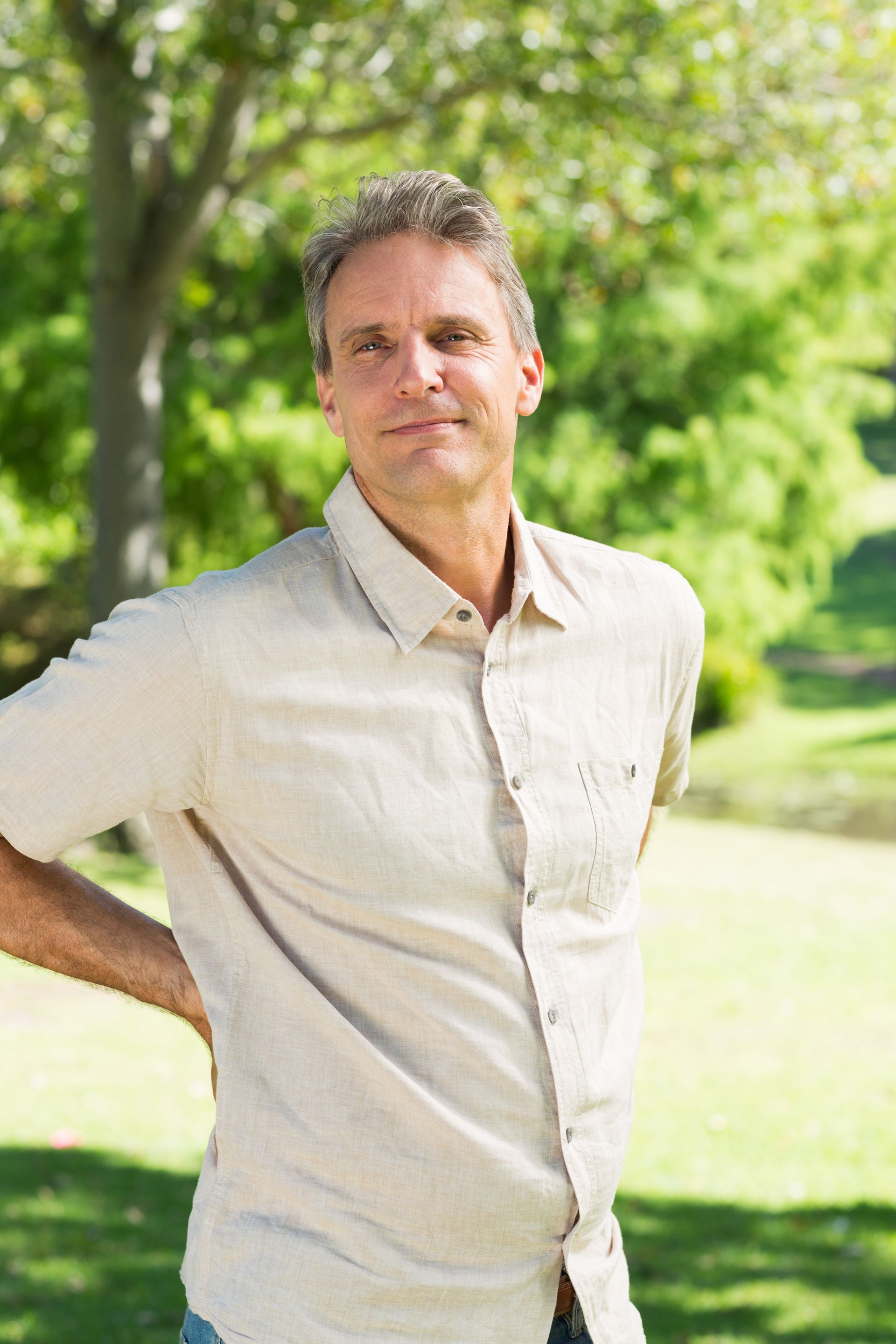 A man is standing in a park with his hands on his back.