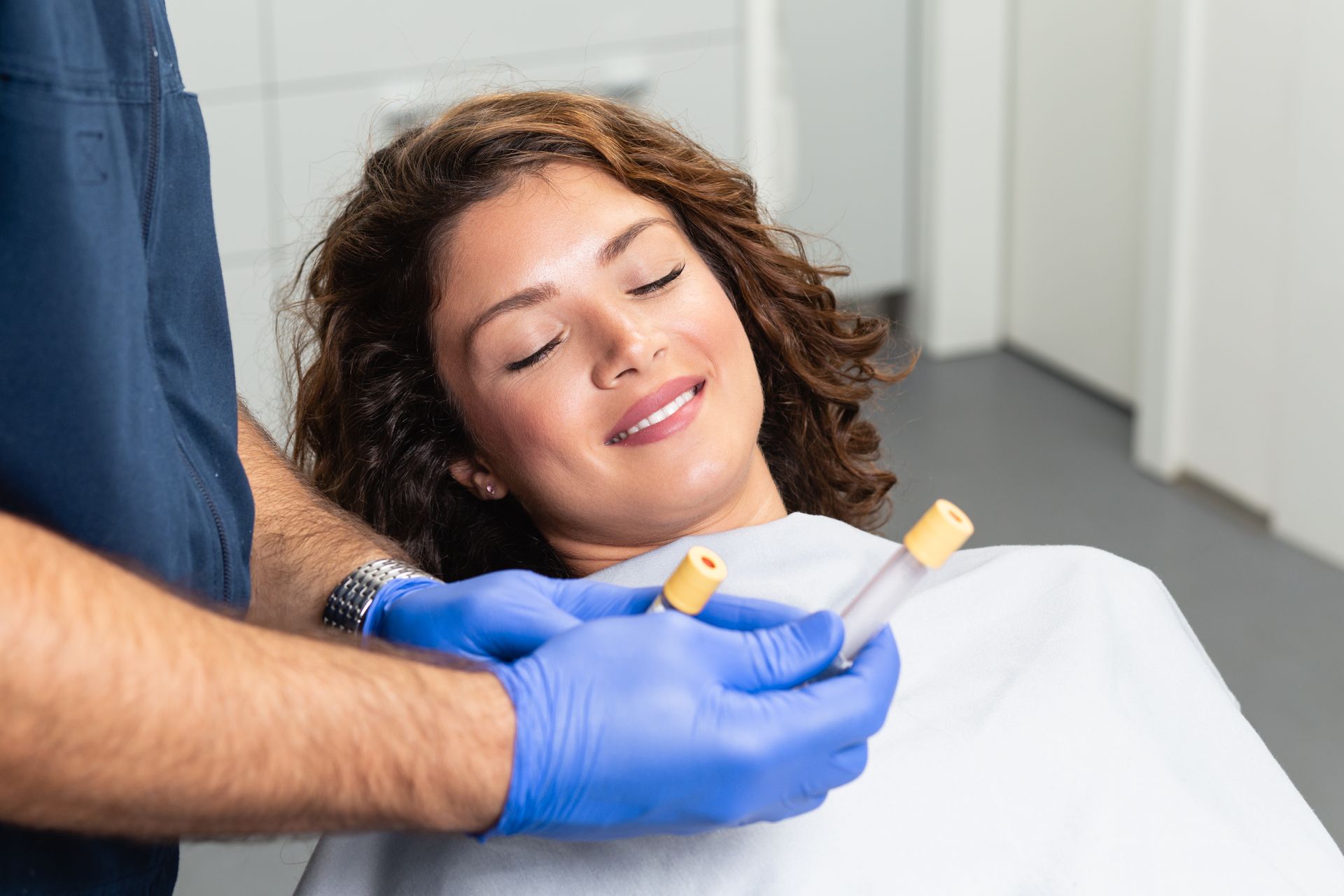 A woman is sitting in a chair with her eyes closed while a doc is holding two test tubes.