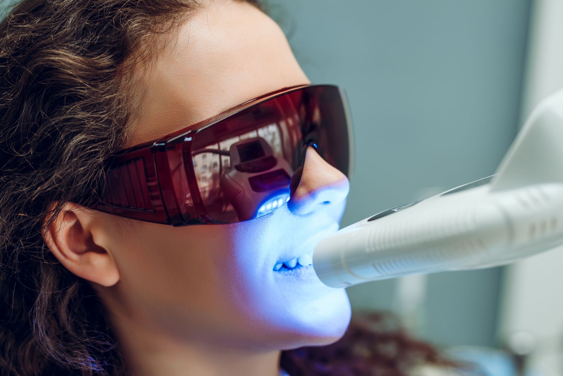Woman with protective eyewear undergoing teeth whitening procedure with a blue light.