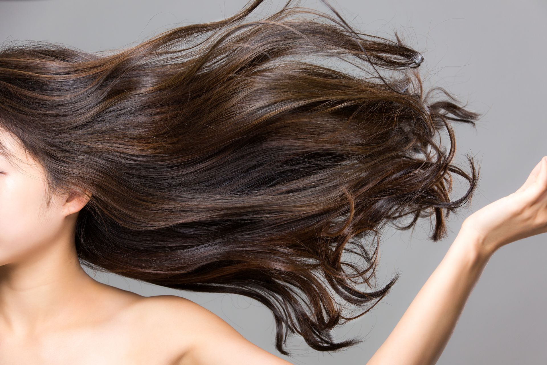 Woman with flowing dark brown hair, arm outstretched, against a gray background.