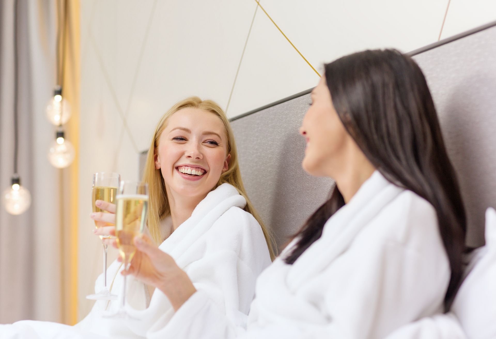 two women in bathrobes are sitting on a bed drinking champagne .