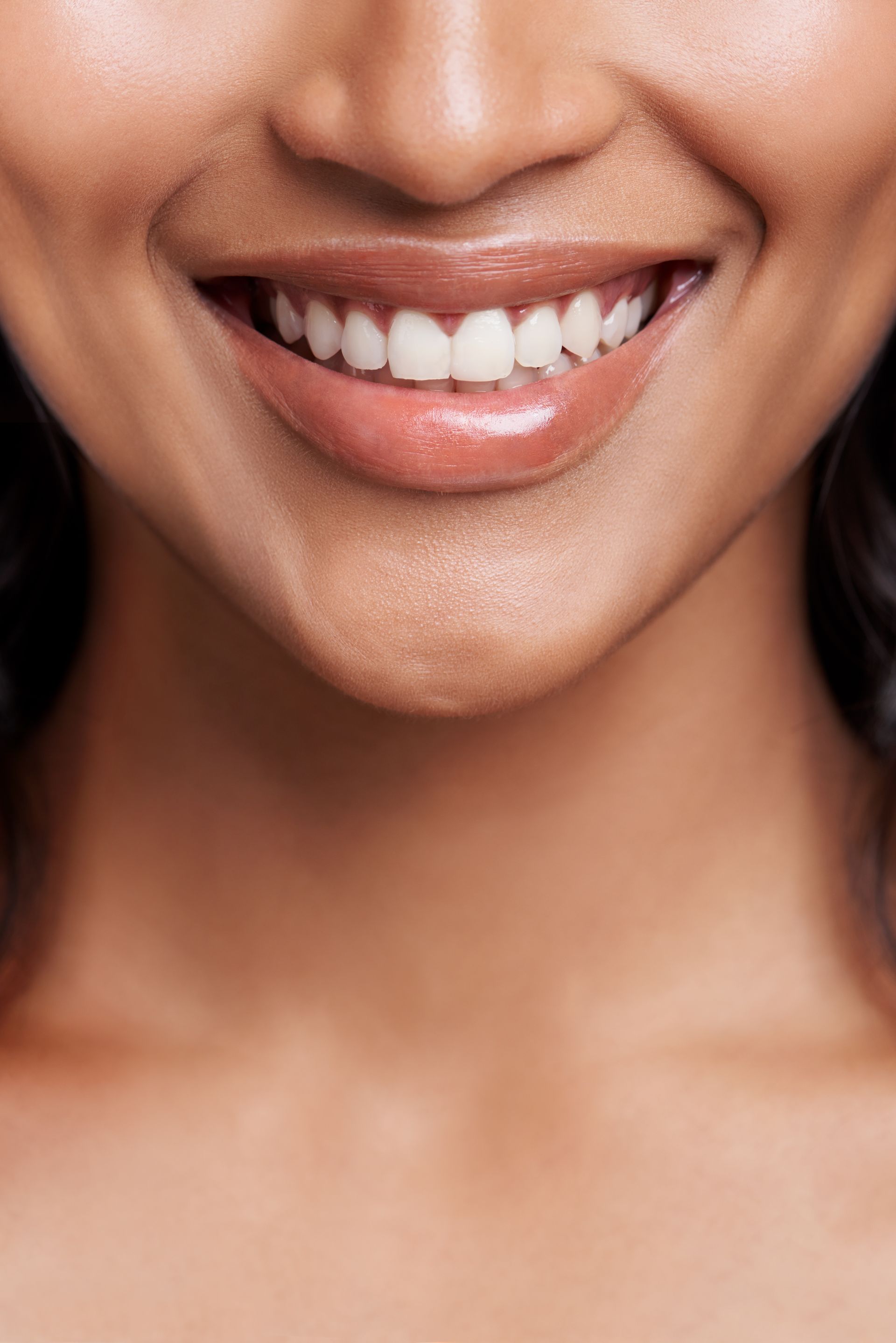 Close-up of a person smiling, showing white teeth and glossy, neutral-toned lips.